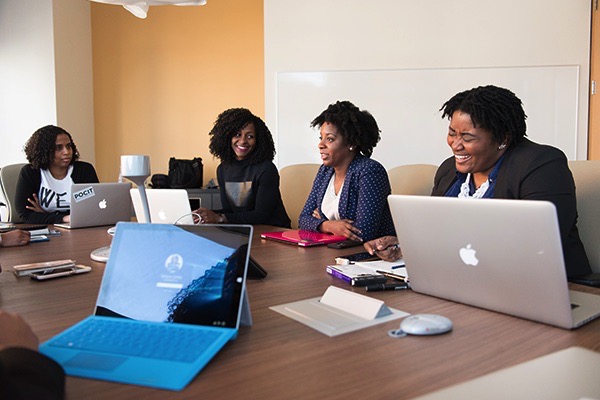 Women seated at a desk with their laptops receiving training on financial wellness for women.