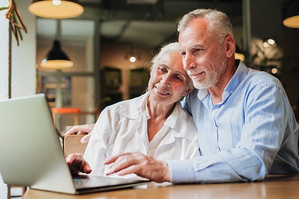 An elderly couple seated at a desk with their laptop while planning for retirement.