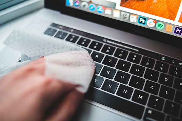 A wet wipe being used to disinfect a laptop keyboard.